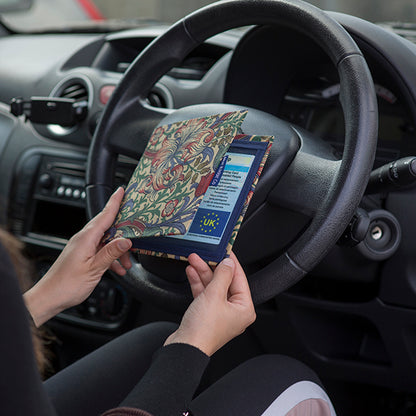 The Blue Badge Wallet is held slightly open, in two hands, against a steering wheel.